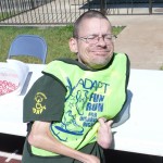 Bryson Smith leans back against a table. He is wearing his green FunRun vest and a big smile.