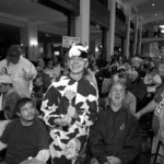Hotel lobby is crammed full of ADAPT protesters. In front a man in a cow suit is surrounded by folks in wheelchairs