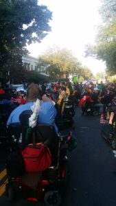 Large group of activists, many in wheelchairs gathered in front of a fancy house.  Shot from the back.