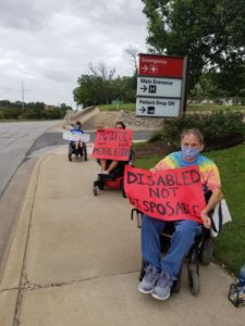 3 people in wheelchairs hold signs by entrance to St David's Hospital South Austin. First sign: Disabled not disposable. Other sign: Justice for Michael Hickson 6-6-73 to 6-11-20.