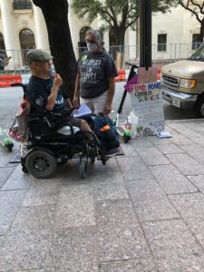 A man in a wheelchair talks with a woman standing beside him on sidewalk