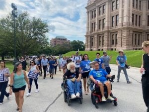 Two wheelchair users in front of crowd marching by front of the Capitol.