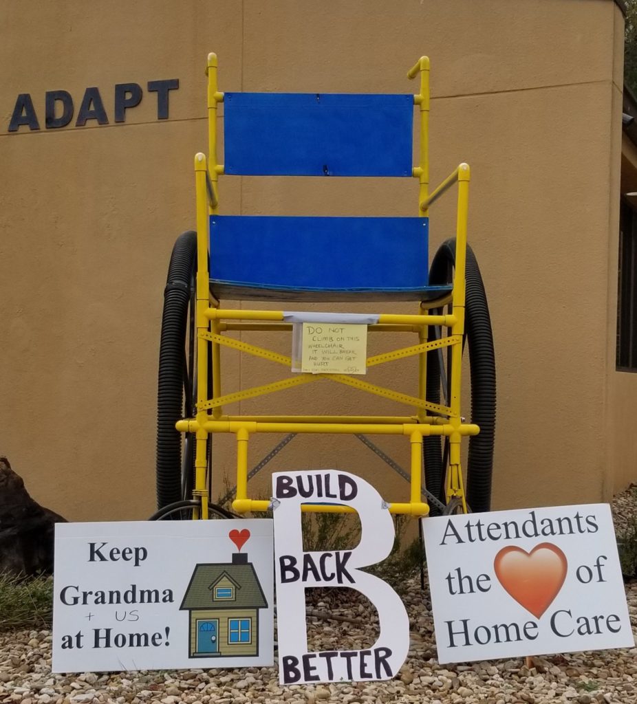 Shows the signs for the BBB action in front of ADAPT's giant 10 foot wheelchair. 
