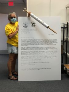 Cathy holds props for action, letter as tall as her and 3 foot syringe
