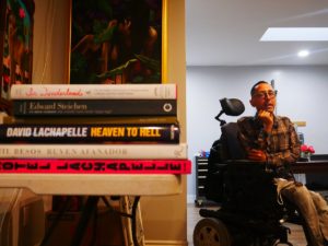 Man in motorized wheelchair in the background and pile of books in the foreground.