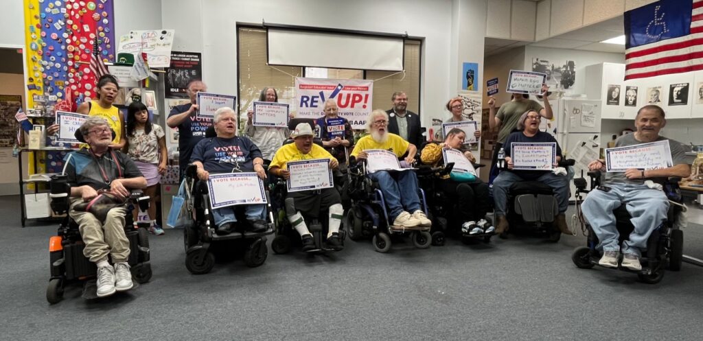 Picture of the Austin group holding signs about why they vote, Behind them is a REV UP banner 