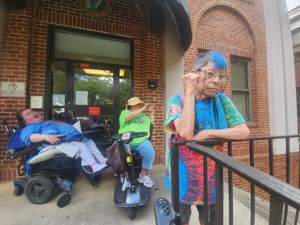 Woman with blue hair and two women in chairs blocking door.