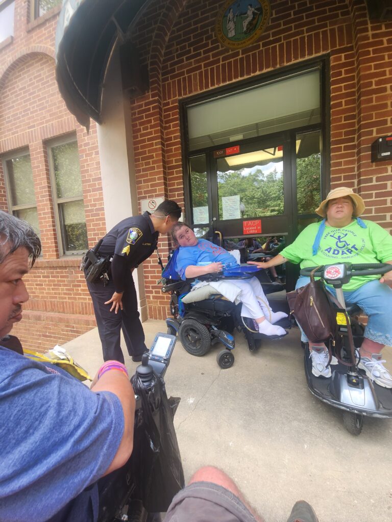 Cop talking to woman in wheelchair blocking HHS door.