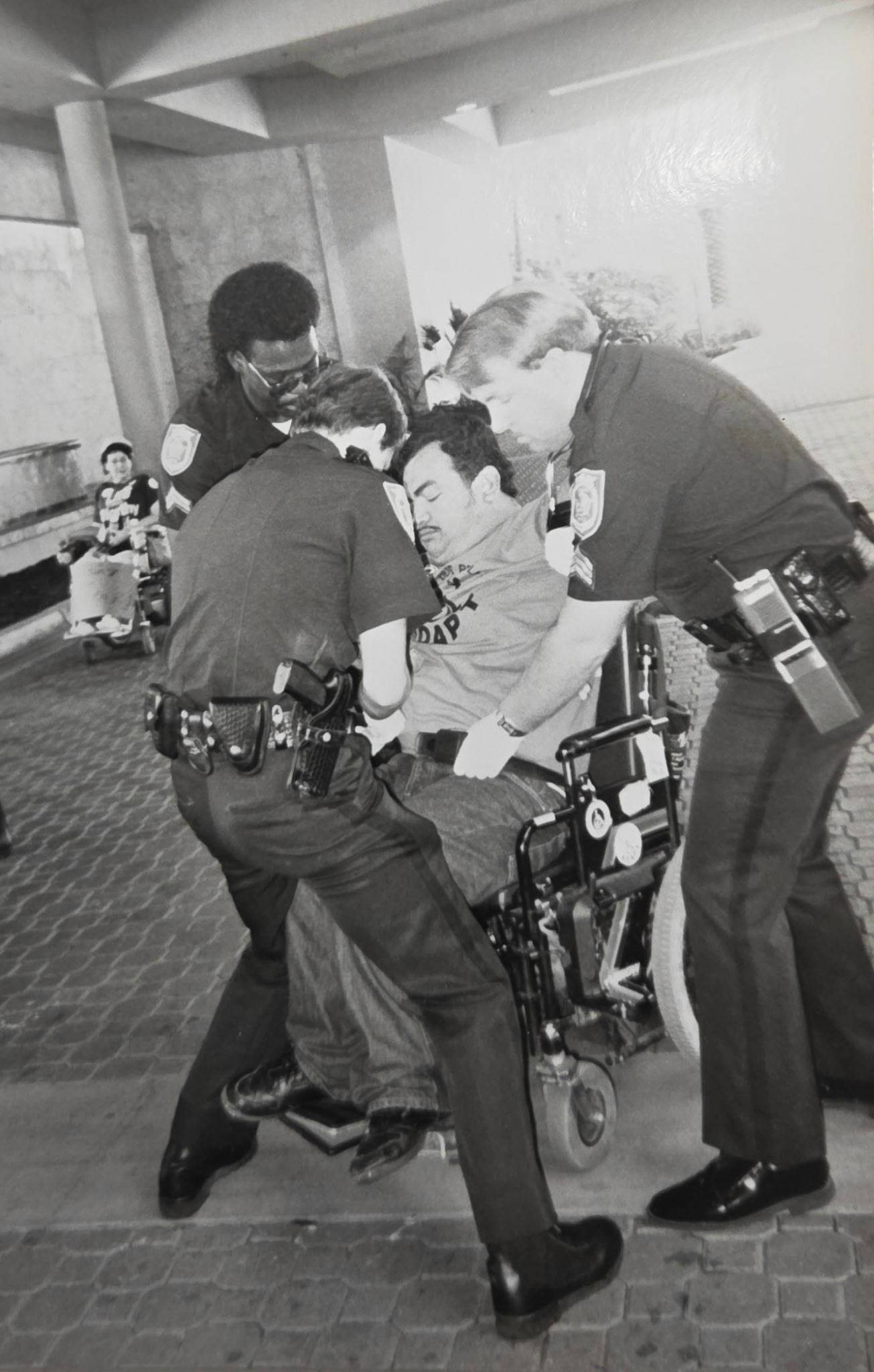 Danny Saenz in his motorized wheelchair is surrounded by three police officers  who are arresting him.